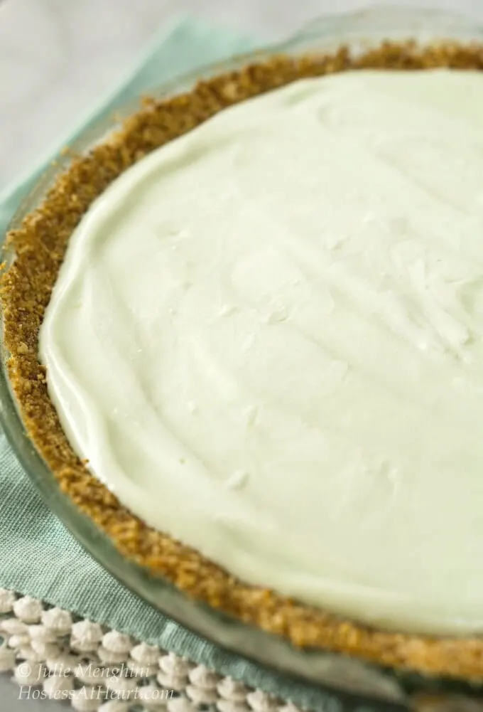 3/4 photo of an uncut Magic Margarita Pie with green tinted whipped topping filling sitting in a crunchy pretzel crust