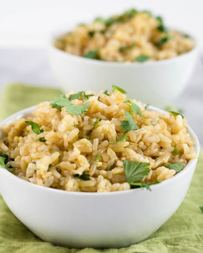 A green napkin topped with a white bowl piled high with tomatillo rice and sprinkled with fresh cilantro. A second bowl sits in the background.