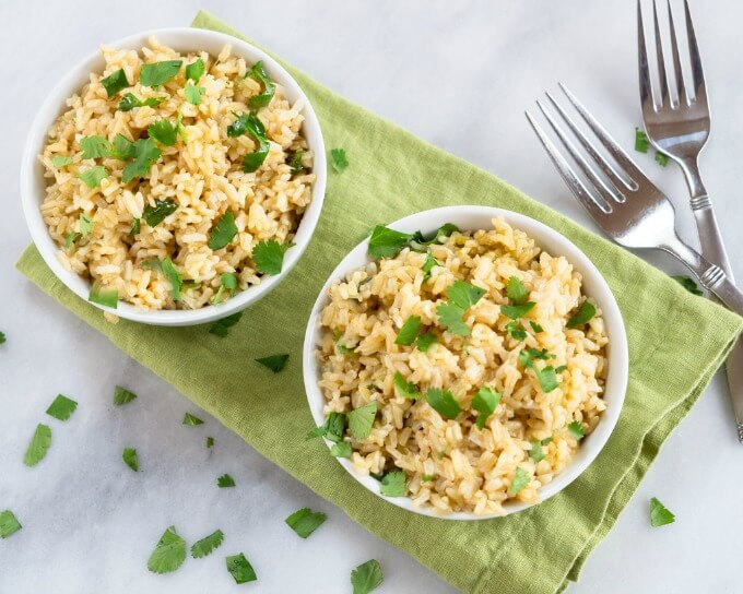 Top-down view of two white bowls of Tomatillo Rice garnished with fresh cilantro on a green napkin next to two forks.