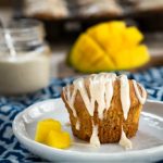 Mango muffin drizzled with vanilla bean glaze on a plate with two pieces of mango.