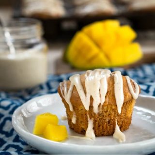 Mango muffin drizzled with vanilla bean glaze on a plate with two pieces of mango.