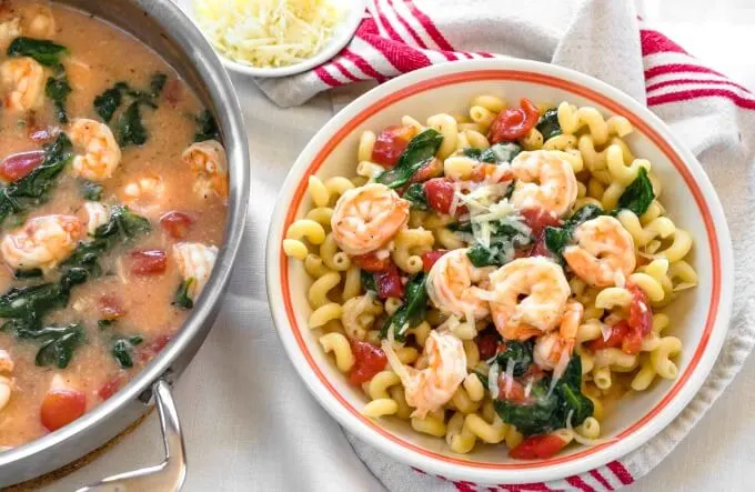 Top view of a bowl of Cavatappi pasta topped with cooed shrimp, spinach, tomatoes and grated cheese
