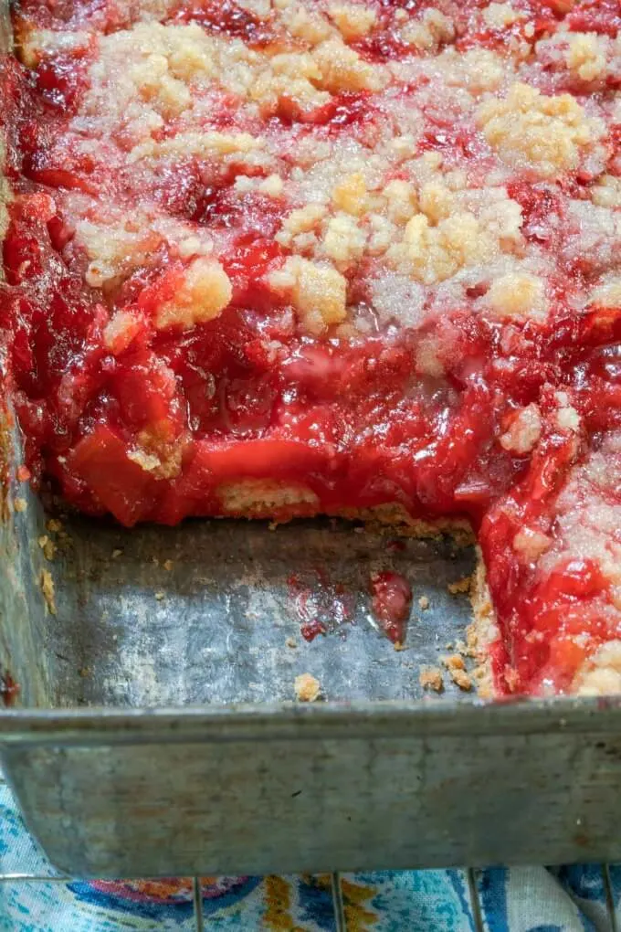 Pan with a missing piece shows the thick red rhubarb filling, pie crust bottom, and crumbled topping.
