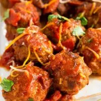 Meatballs on a white plate covered with a red spicy chipotle sauce and sprinkled with cheese and fresh green cilantro