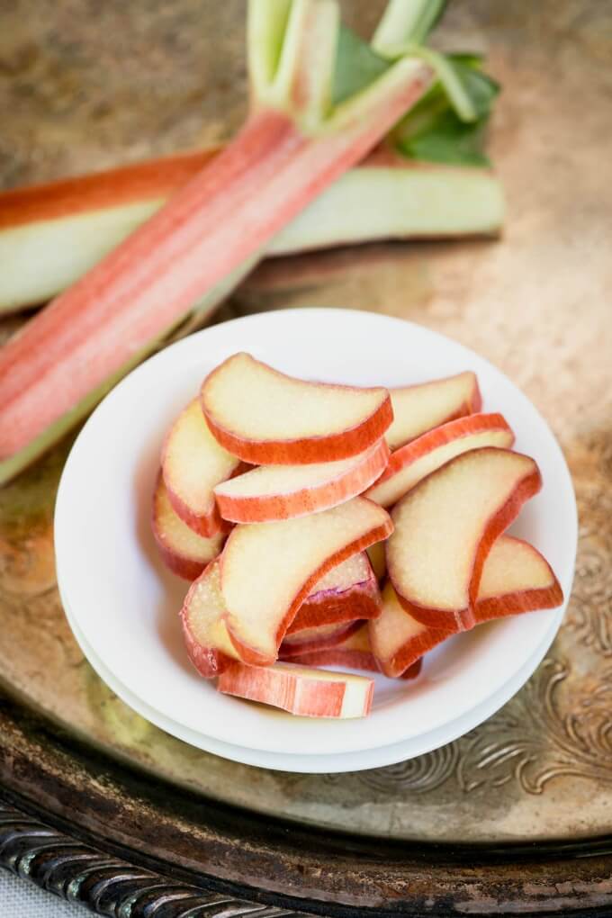 Fresh sliced rhubarb in a white bowl with stalks of rhubarb on an antique tray.