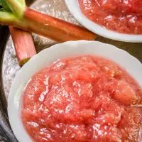 Top view of two dishes of sweet tart rhubarb sauce on an antique tray with stalks of fresh rhubarb