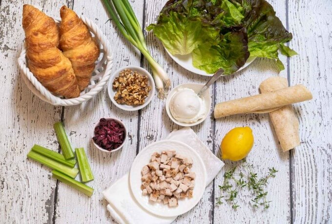 Ingredients for Chicken salad including lettuce, diced chicken, yogurt, lemon, celery, crasins, walnuts, and onions