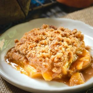 Peach crisp with a crunchy streusel topping sitting on a white plate and the pan in the background