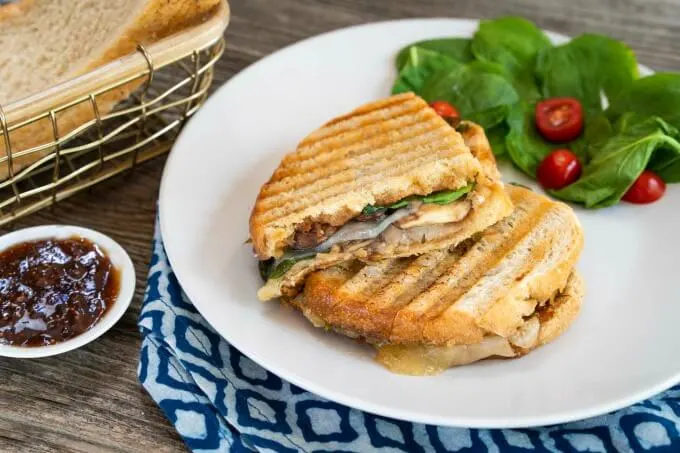 Grilled Cheese panini sandwich cut in half next to a spinach tomato salad on a white plate over a blue patterned napkin.