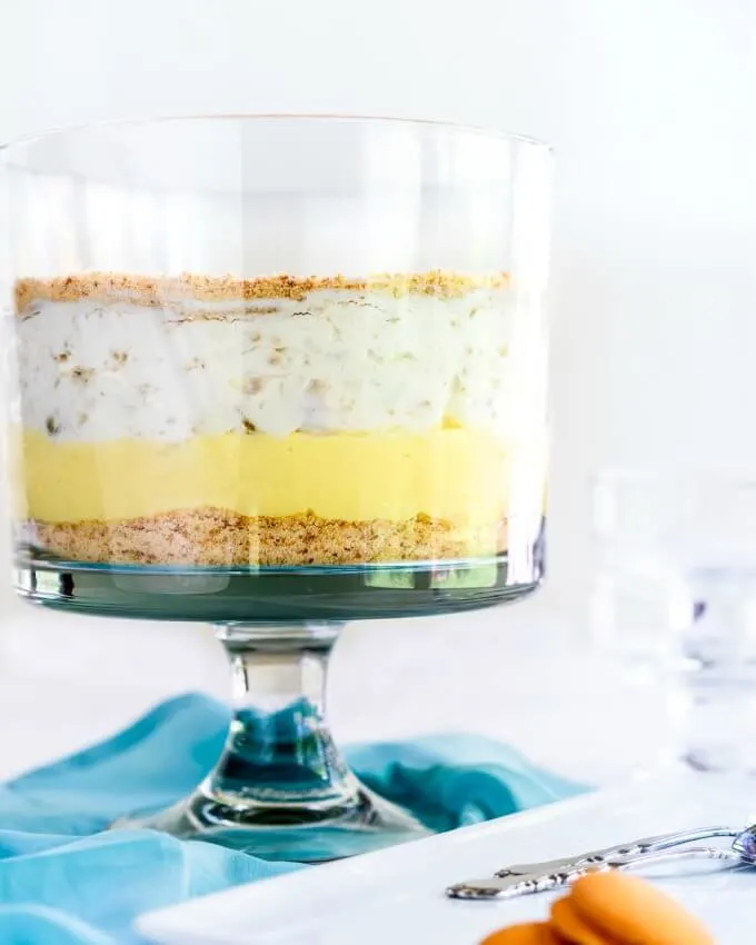 Side view of a trifle bowl filled with layers of ground cookies, pudding, and fruit-filled whipped topping on a turquoise napkin.