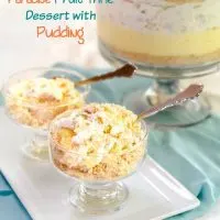Two dessert dishes filled with a mound of fruit-filled whipped topping, cookie crumbs, and vanilla pudding sitting on a white tray. The trifle bowl filled with the dessert sits in the background over a turquoise napkin. The title 