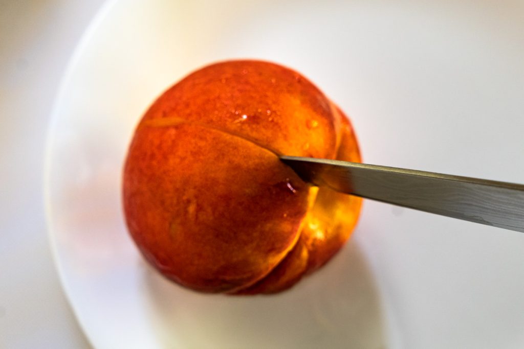 A peach being scored with a sharp knife.