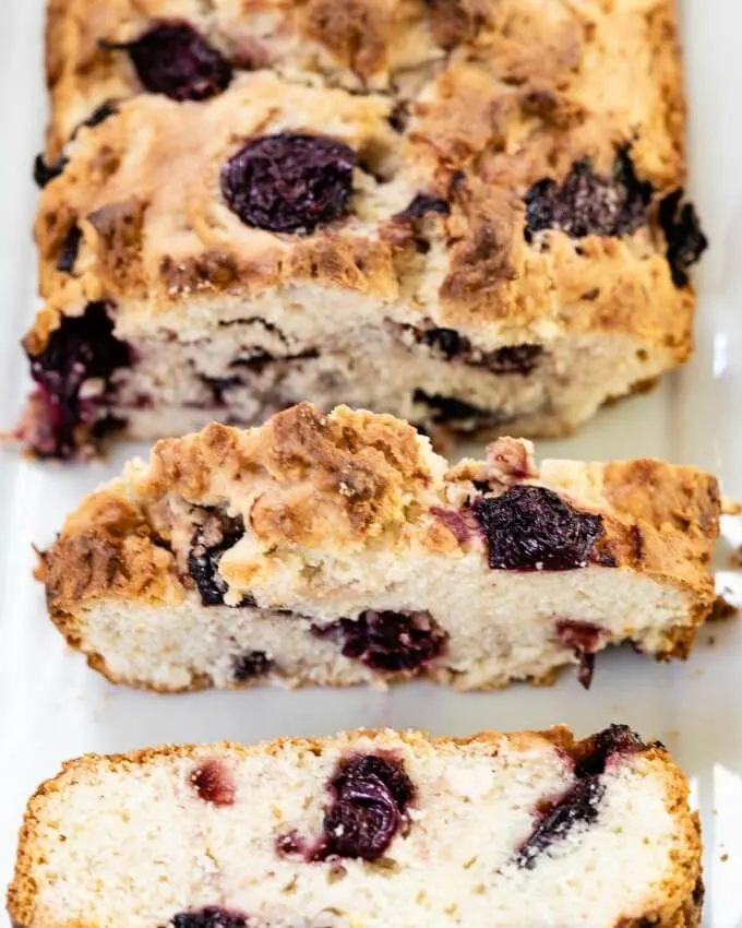 Top-down view photo of a sliced loaf of Cherry Quick bread sitting on a white plate.