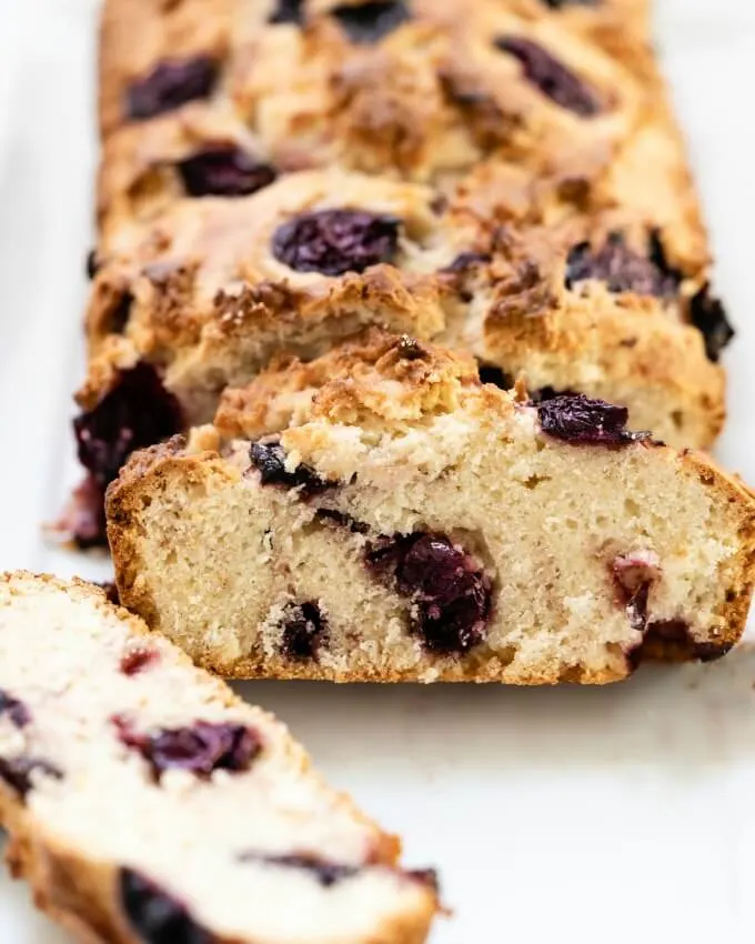 Close up of a slice of quick cherry bread loaded with dark purple cherries.