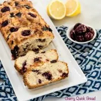 Cherry Bread loaf on a white plate sitting on a blue napkin next to lemons and cherries