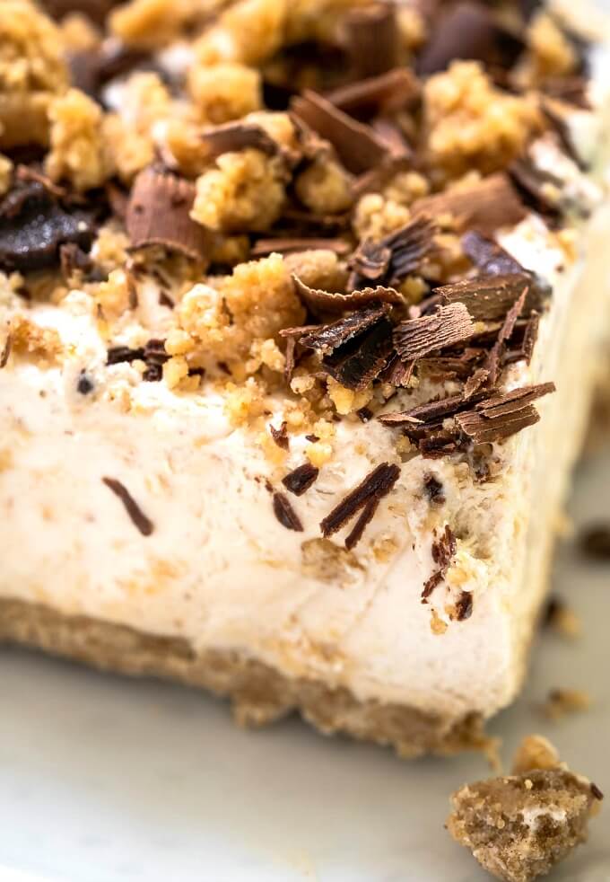 Corner of a piece of frozen peanut butter cheesecake topped with brown sugar peanut butter crumble and shaved chocolate