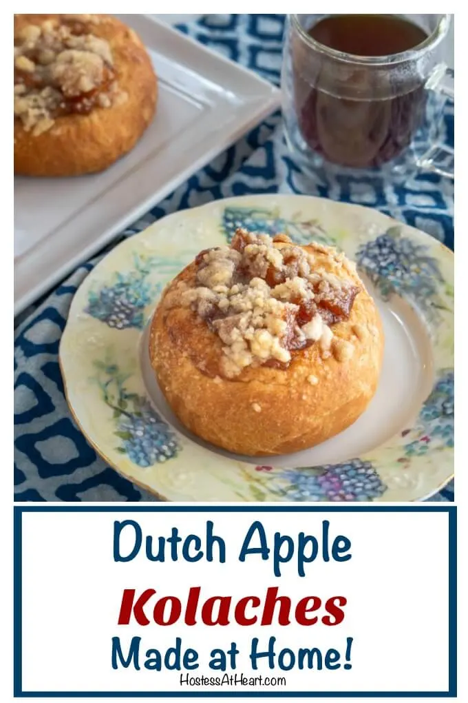 Baked roll filled with apple filling and topped with a cinnamon crumble sitting on a floral plate in front of a cup of coffee and tray of rolls.