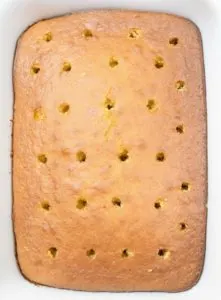 Baked cake with holes punched into the top in a white baking dish
