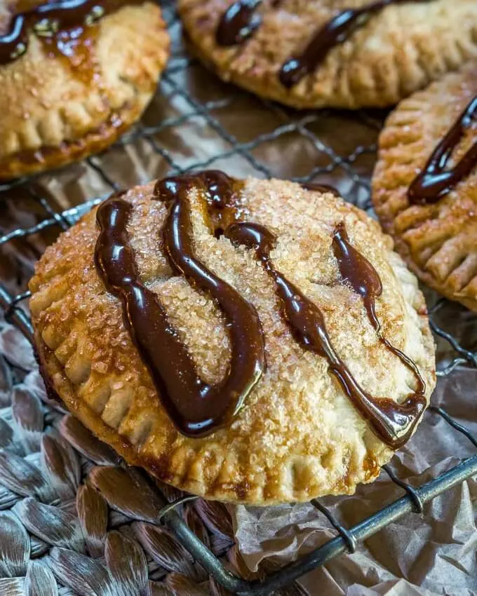Close up of a golden brown baked hand pie sitting on a baking rack drizzled with dark chocolate.