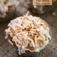 Top shot of a muffin in a silver paper topped with toasted coconut with two muffins in the background. The title 