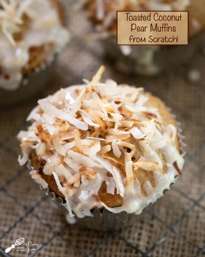 Top shot of a muffin in a silver paper topped with toasted coconut with two muffins in the background. The title \"Pear Muffins From Scratch\" appear in the top right of the photo.