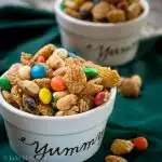 Close up of Crispix snack mix loaded with m&ms and peanuts sitting on a green napkin dotted with spilled snack mix