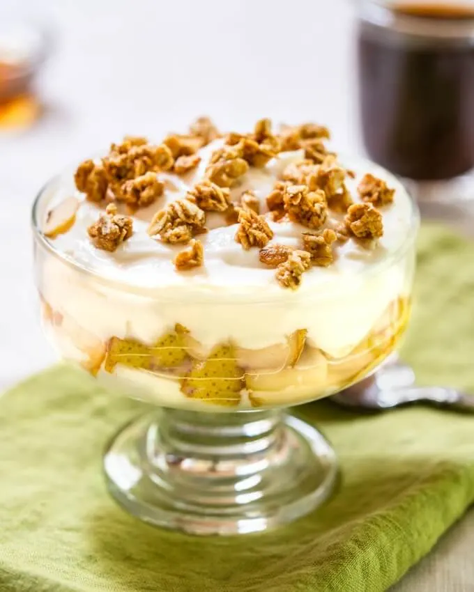 Glass dish with layers of yogurt and diced pears sprinkled with granola on top sitting on a green napkin