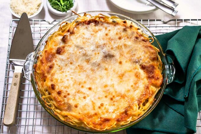 A pie plate full of spaghetti pie and baked brown. It's sitting on a cooling rack next to a green napkin and pie server.