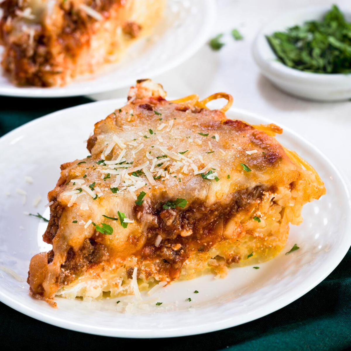 Close up of a slice of spaghetti pie showing layers of pasta and sauce topped with mozzarella and baked brown sitting on a white plate.