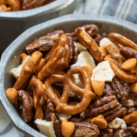 Close up view of pretzels, pecans, caramel chips and dried apples mix in a bowl on a blue striped napkin