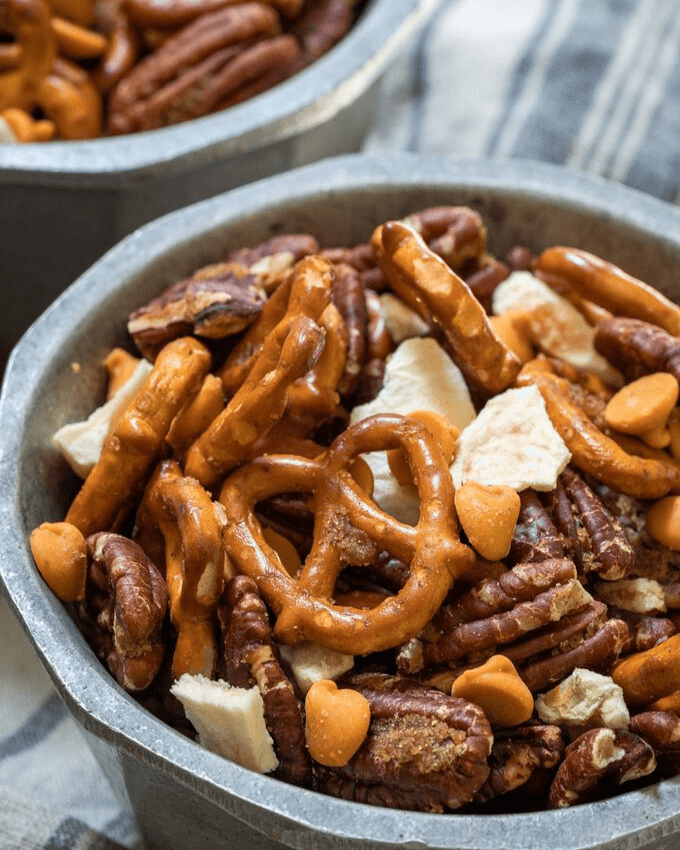 Close up view of pretzels, pecans, caramel chips and dried apples mix in a bowl on a blue striped napkin