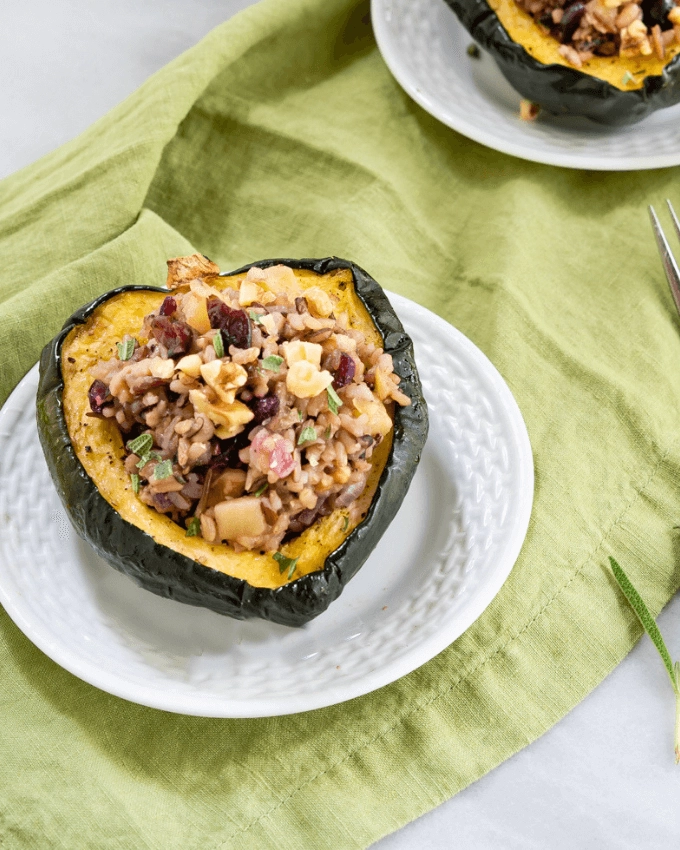 Close up of a half of baked acorn squash filled with wild rice and apple sitting on a white plate over a green napkin.