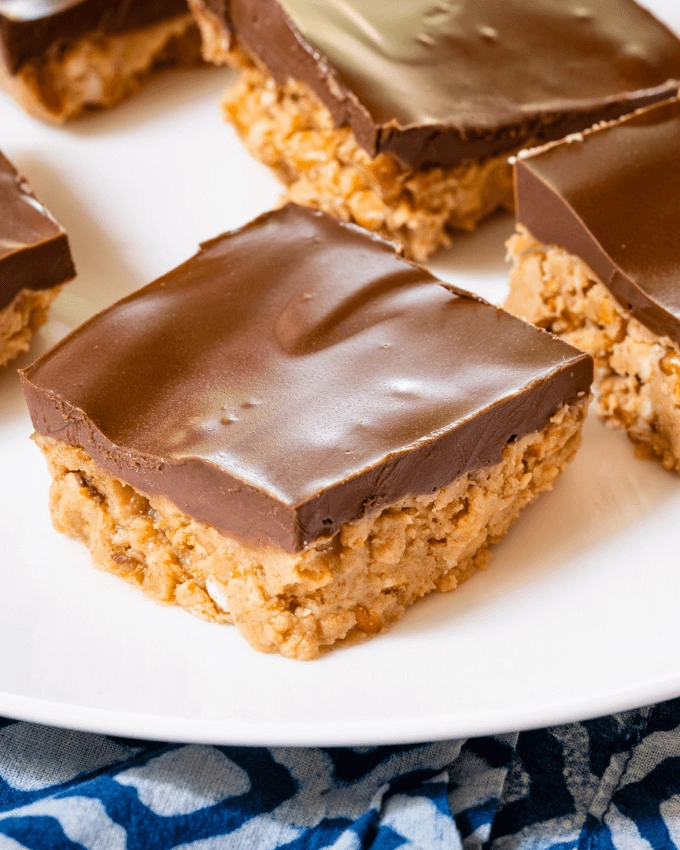 Top view of a pretzel dessert topped with milk chocolate on a white plate surrounded by other pieces.