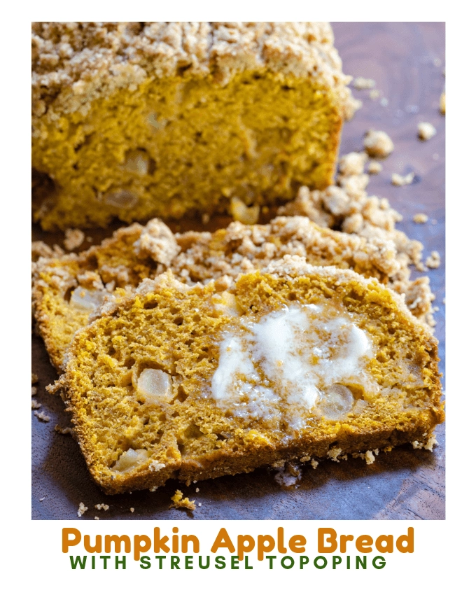 A slice of pumpkin bread dotted with chunks of apple and streusel topping with melted butter running down the slice over a wooden cutting board.
