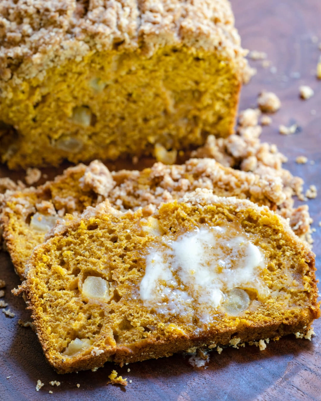 Pumpkin bread dotted with chunks of apple and streusel topping with melted butter on a slice