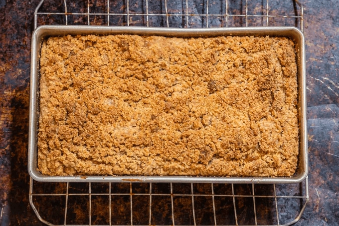 Top shot of a bread pan filled with pumpkin apple bread topped with streusel topping. This bread sits on a cooling rack over a brown sheet pan.