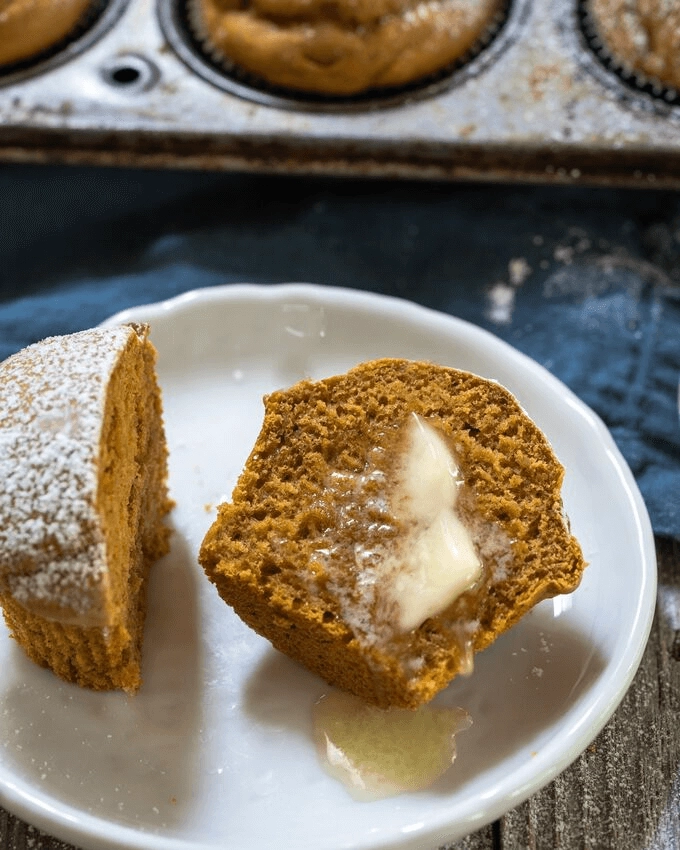 Top view of a pumpkin muffin sliced in half and slathered with melting butter on a white plate.