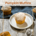 Angle photo of a powder sugar dusted pumpkin muffin sitting on a white plate surrounded by other muffins in front of a tin of muffins.
