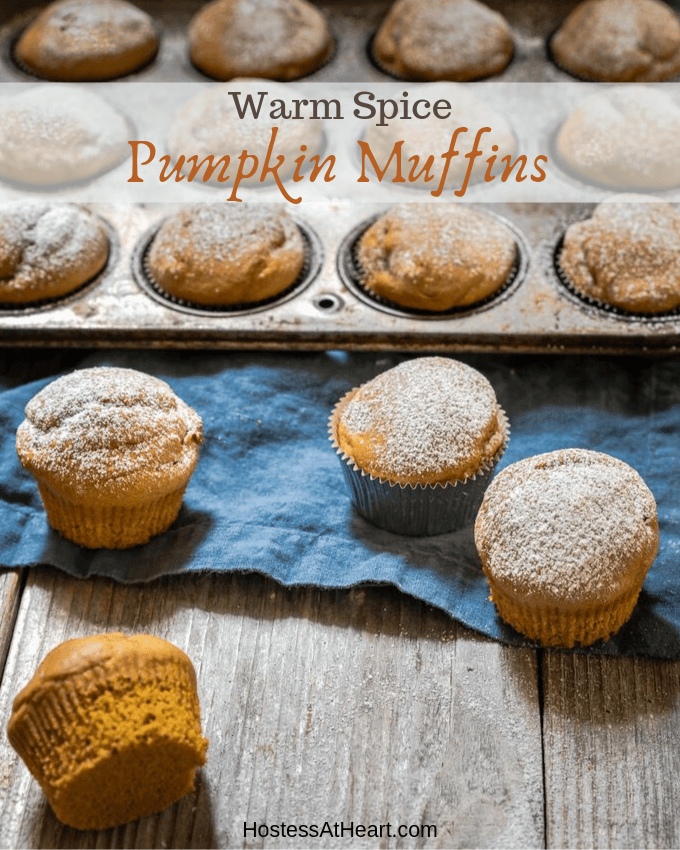 FAngle view of mini pumpkin muffins dusted with powdered sugar sitting on a blue napkin and wooden board in front of a tin of muffins. The title \"Warm Spice Pumpkin Muffins\" runs across the top of the photo.