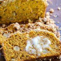 Pumpkin bread dotted with chunks of apple and streusel topping with melted butter on a slice