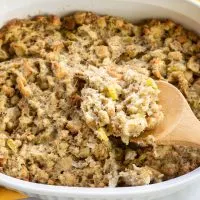 A spoon lifting baked Thanksgiving dressing from a casserole dish