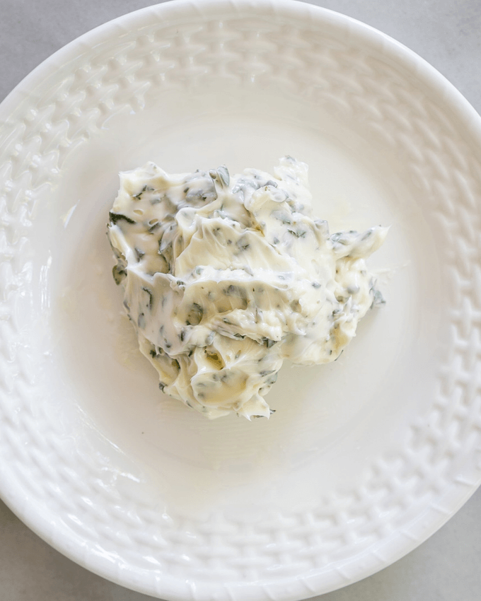 Butter mixed with green herbs on a white plate with recipe title across the bottom