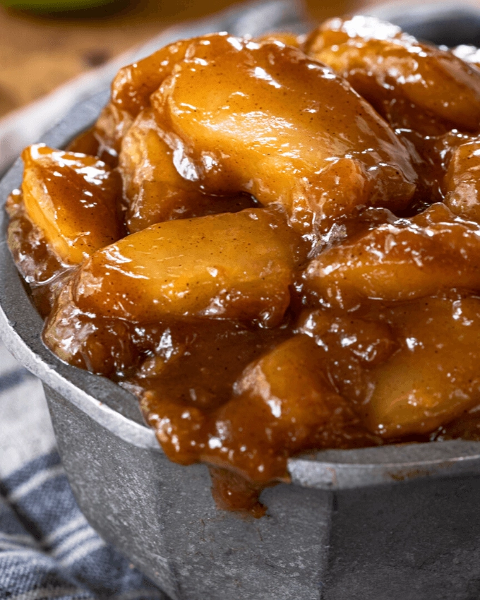 Straight on view of apples in brown sugar-cinnamon sauce overflowing a metal bowl.