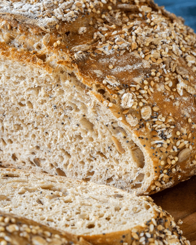 Close-up photo showing the holes in the crumb and a browned crusty exterior topped in a multi-grain blend of seeds and oats.