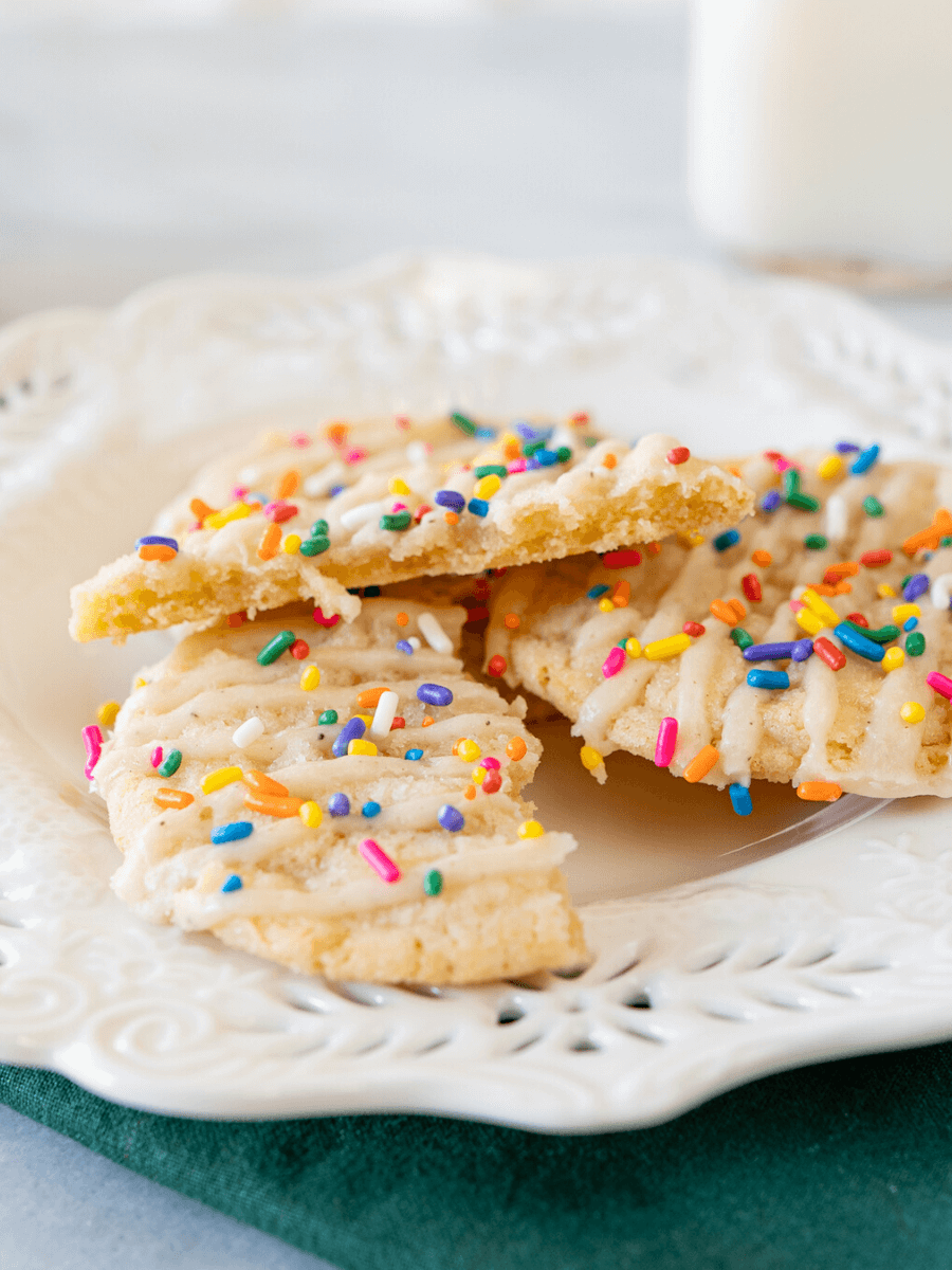 Close up side photo of a broken glazed cookie with sprinkles on a white plate showing the soft center.