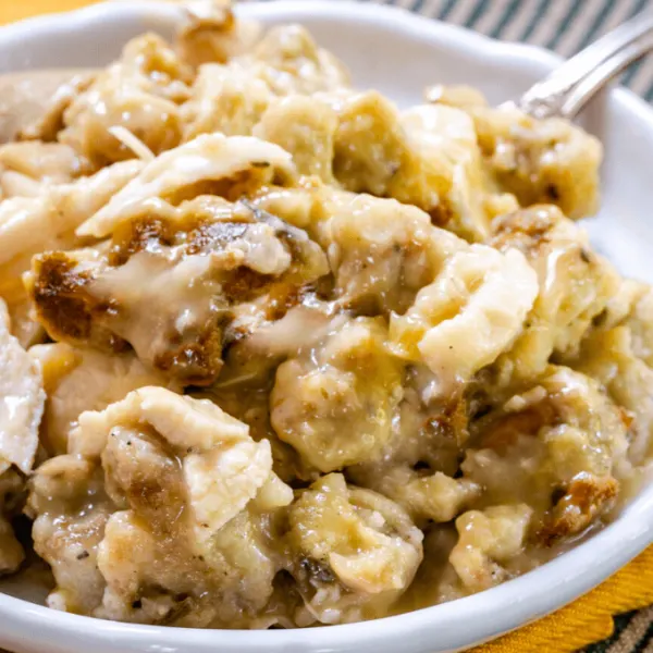 45 degree angle of a casserole made of turkey and dressing in a chicken soup on a white plate sitting on a white plate sitting on a gold napkin.