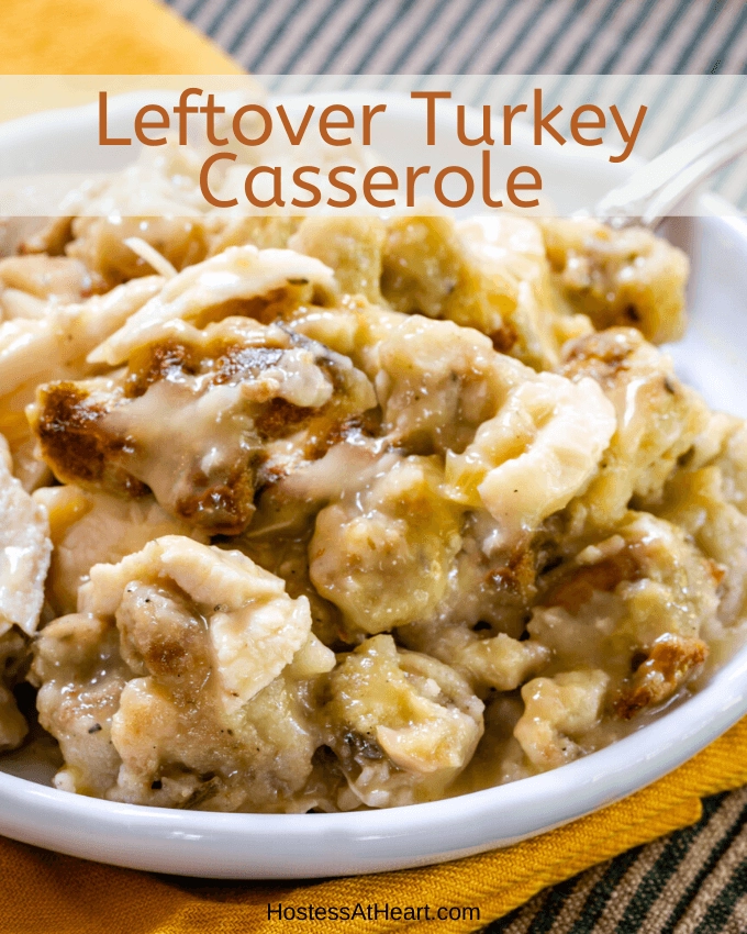 Chunks of leftover turkey and dressing in creamy chicken soup on a white plate sitting on a gold napkin and a green striped napkin with the title \"Leftover Turkey Casserole\" over the top.