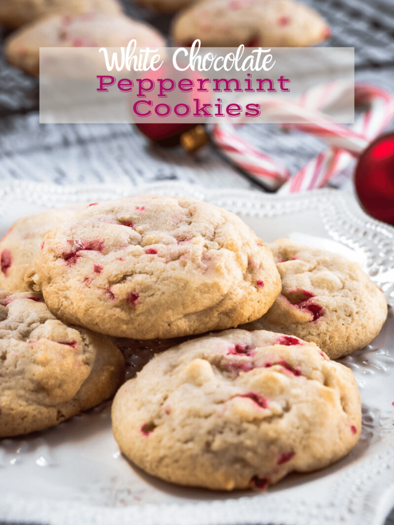 Stack of cookies on a white plate with a cooling rack filled with cookies, Christmas bulbs & candy canes behind it.