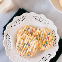 Top looking down at three sugar cookies layered over each other on a white plate on a marble background in from on milk and more cookies.
