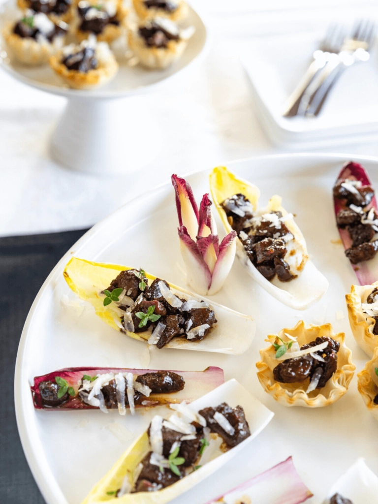 top down view of 3/4 serving tray of endive lettuce leaves filled with pieces of lamb and sprinkled with pecorino cheese and fresh thyme.